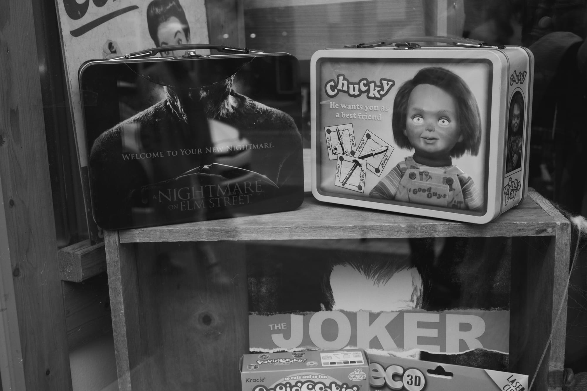 Two lunchboxes featuring Chucky the doll and Freddy Kruger sit in a store window.